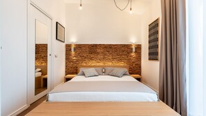 Un dormitorio moderno con cabecera de madera, cama grande, mesitas de noche, un espejo y una lámpara de pared.