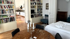 Une pièce comprenant une table à manger en bois, un canapé bleu, un lit et un coin cuisine avec un meuble blanc et un évier.