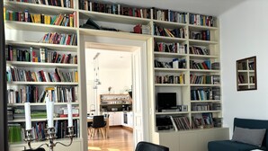 Une pièce bien éclairée, avec une table à manger en bois, un fauteuil en cuir noir, un canapé turquoise et une bibliothèque remplie de livres.