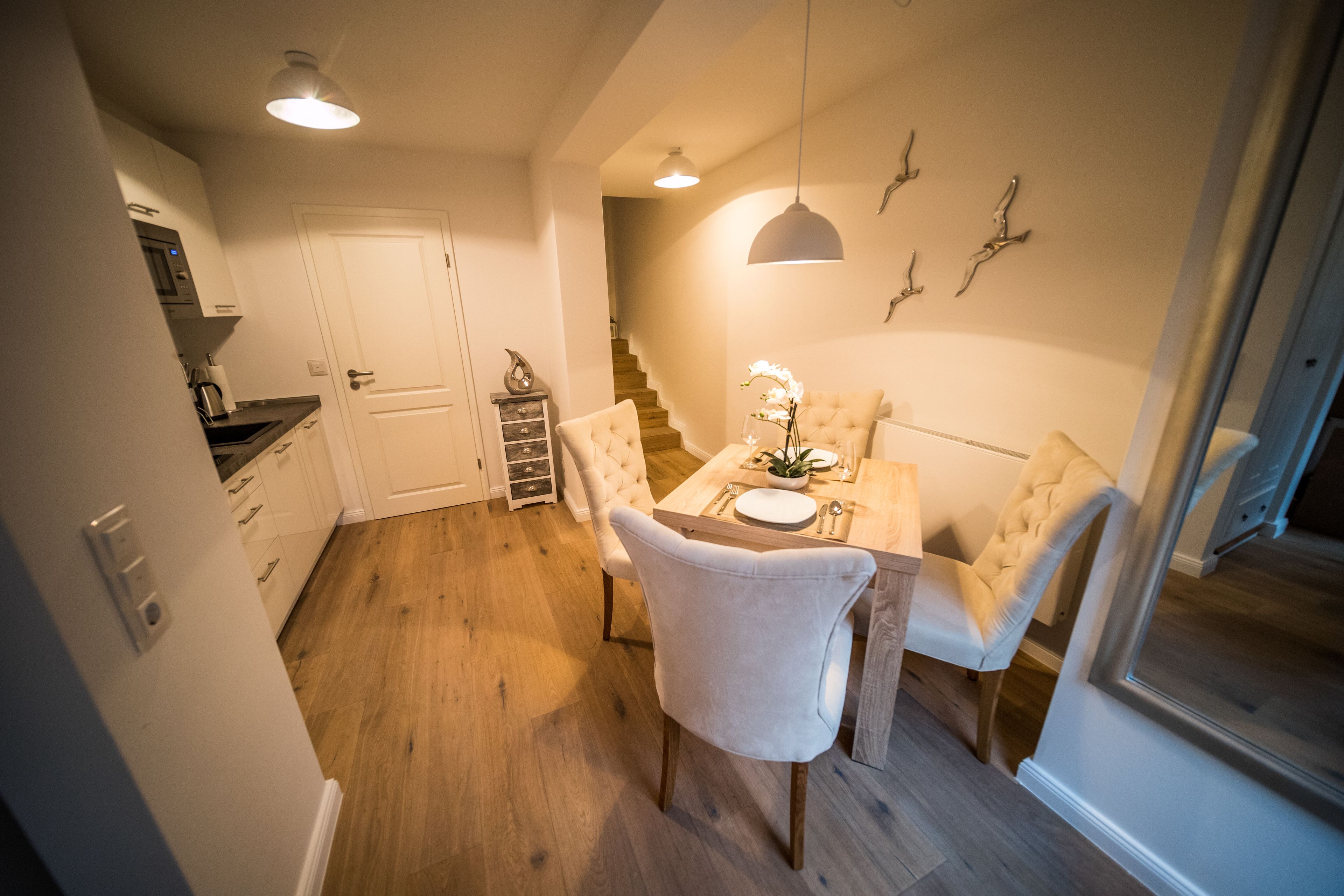 A compact kitchen with modern appliances, a dining area with a white table and chairs, and a staircase leading to another level.