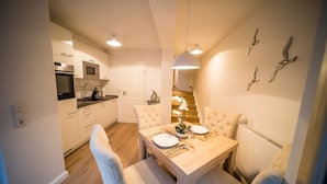 Una cocina moderna con armarios blancos, una mesa de comedor para dos personas y una escalera que conduce a un nivel superior.