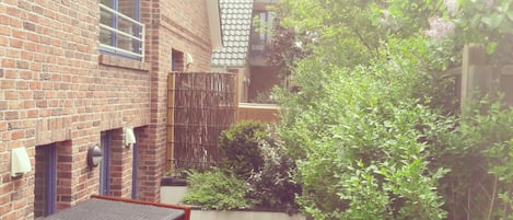A brick building with a white fence, a covered seating area, and greenery.