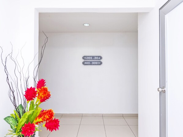 Un couloir avec un mur blanc, une porte sur la droite et un panneau indiquant les numéros de chambre 301 à 304 et 305 à 309.