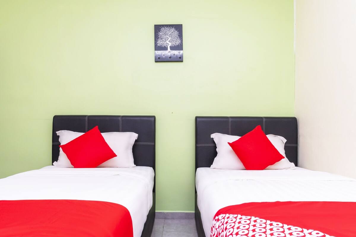 Two single beds with black headboards and red and white bedding, a small framed picture on the wall, and a green wall.