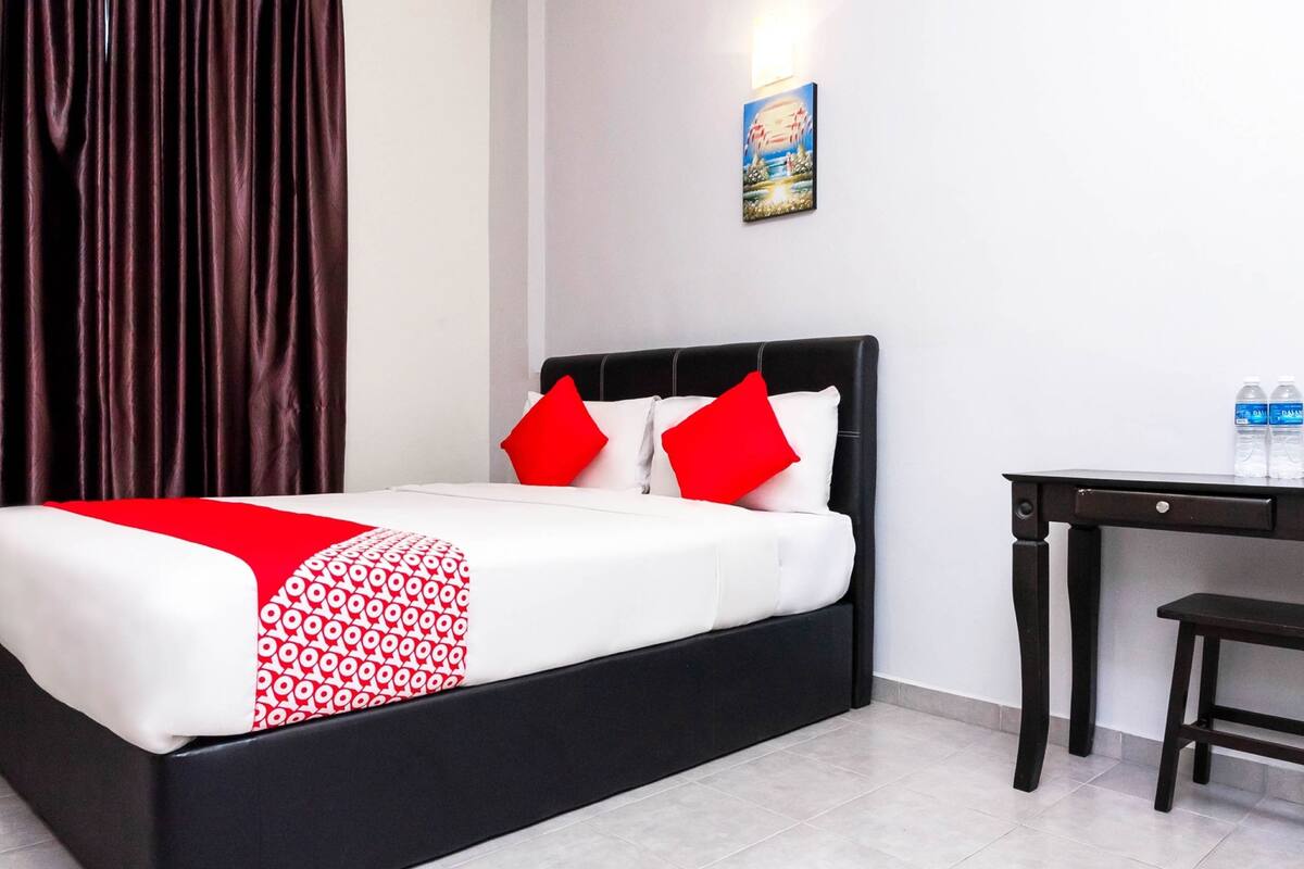 A neatly made bed with a black frame, white bedding, and red accents.