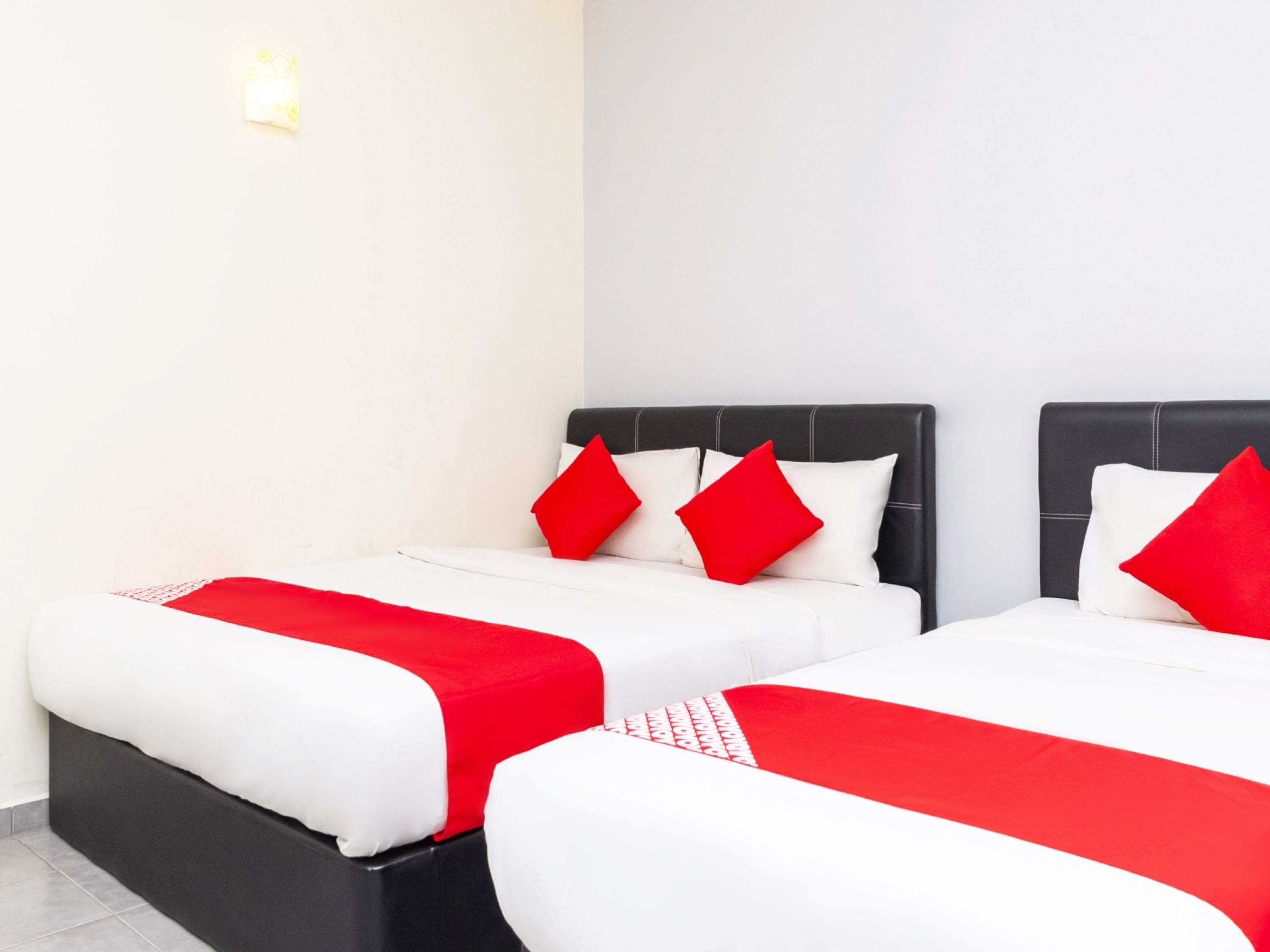 A hotel room with two beds, each with white bedding and red accents, and a black headboard.