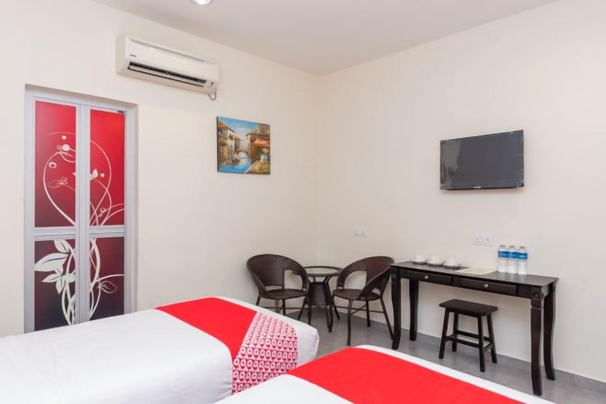 A hotel room with two beds, a desk with chairs, a TV, and a painting on the wall.