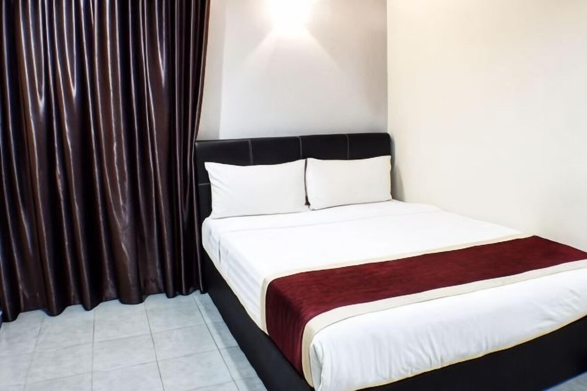 A hotel room with a bed, curtains, and a wall-mounted light.