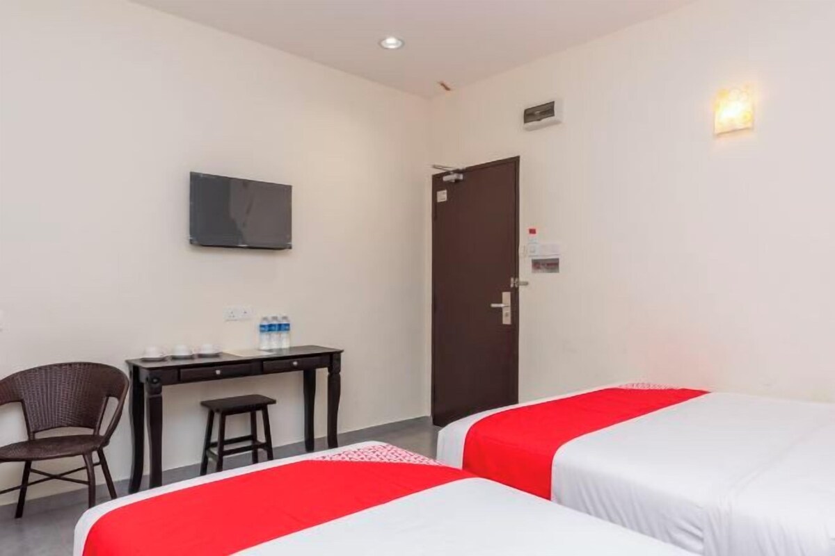 A hotel room with two beds, a desk, a chair, a television, and a door.