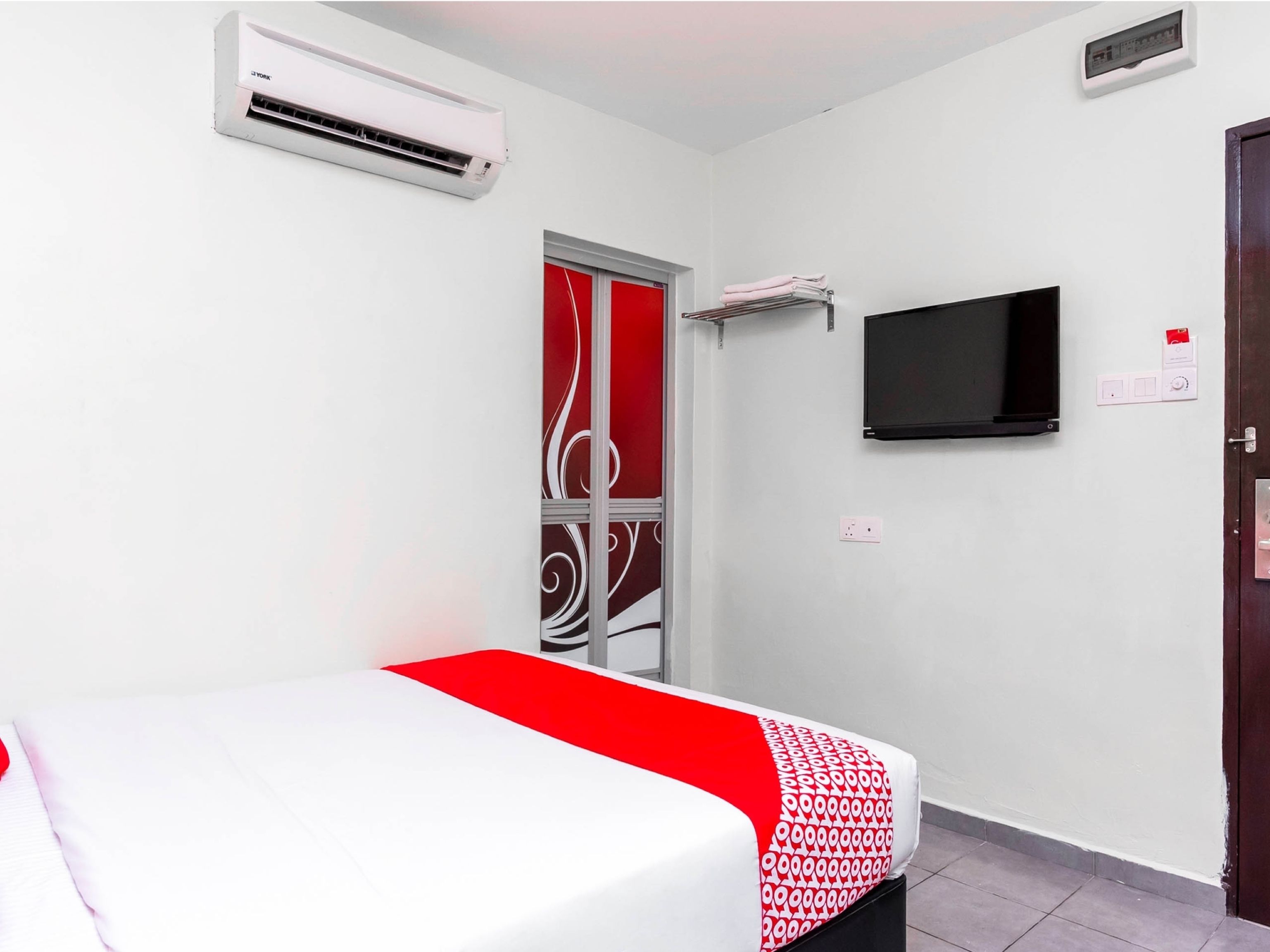 A hotel room with a bed, an air conditioning unit, a television, and a door with a decorative panel.