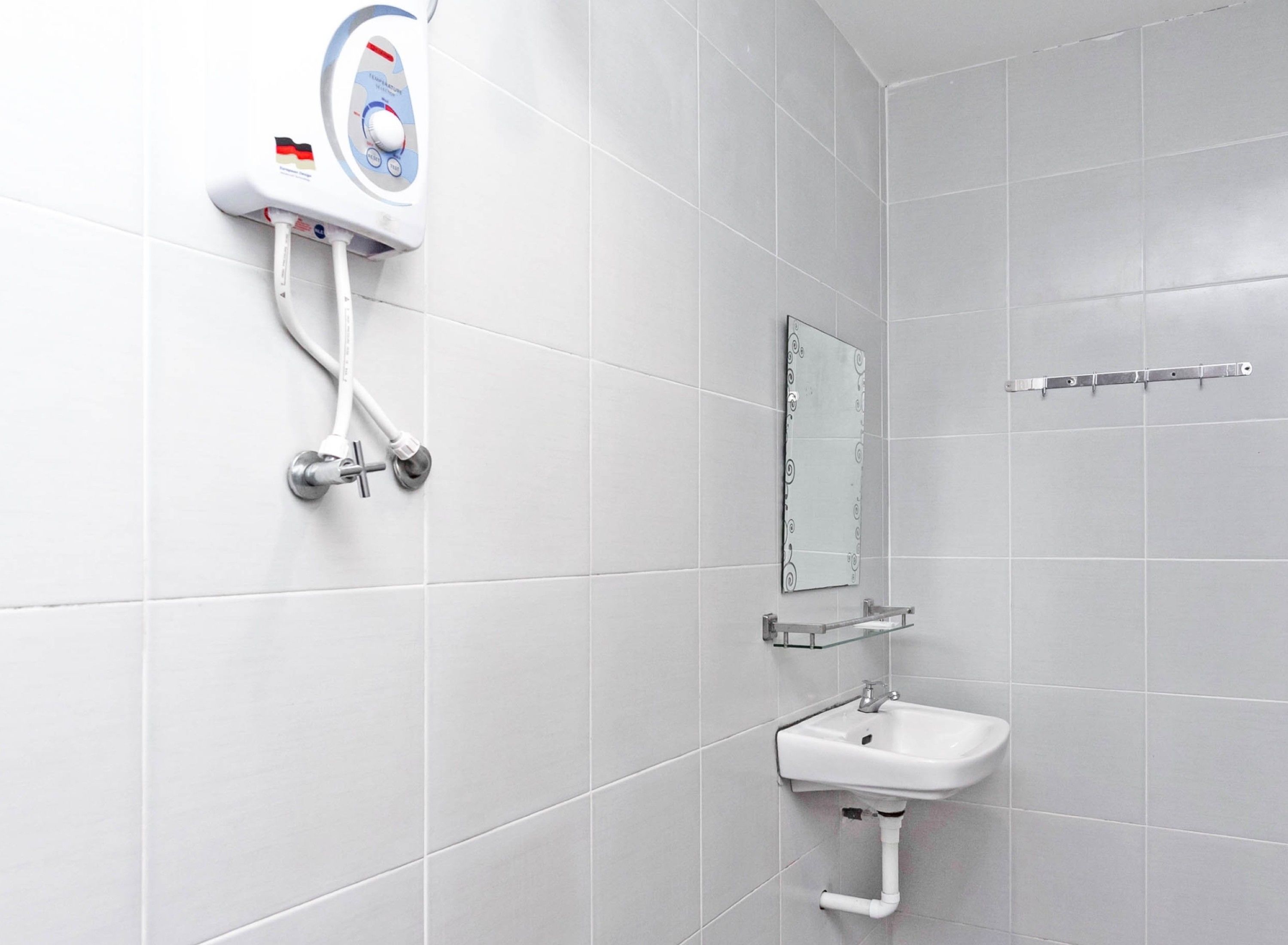 A bathroom with white tiles, a wall-mounted soap dispenser, a mirror, and a sink with a glass shelf.