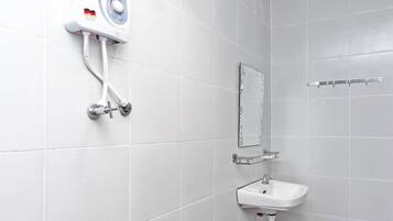 A bathroom with white tiles, a wall-mounted soap dispenser, a mirror, and a sink with a glass shelf.