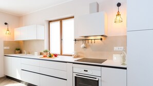 Une cuisine moderne avec des meubles blancs, un four encastré et une fenêtre agrémentée de rideaux.