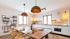Une cuisine moderne avec des meubles blancs, une table à manger en bois et un luminaire suspendu.