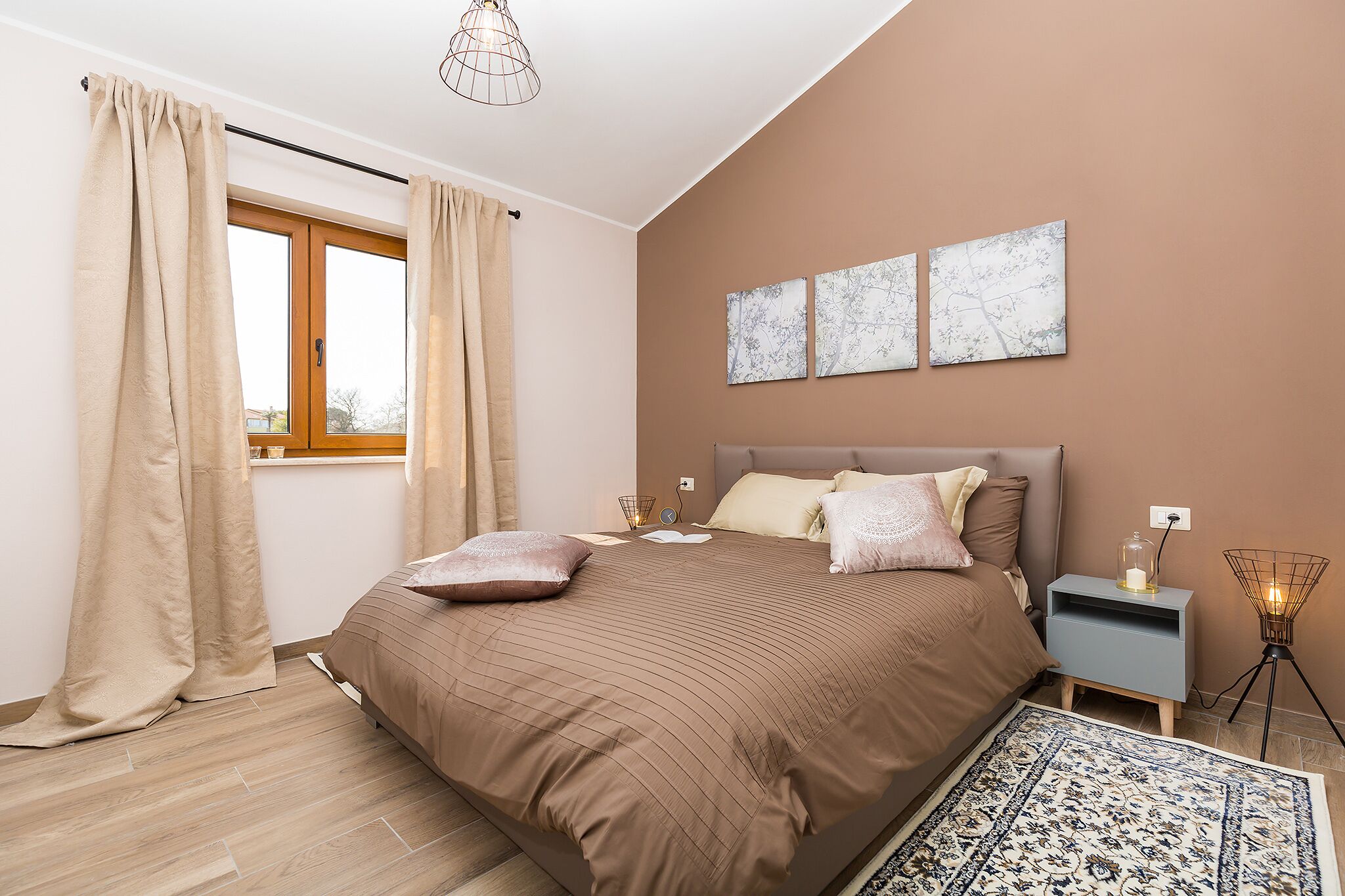 A bedroom with a large bed, a nightstand, a lamp, and a window with curtains.