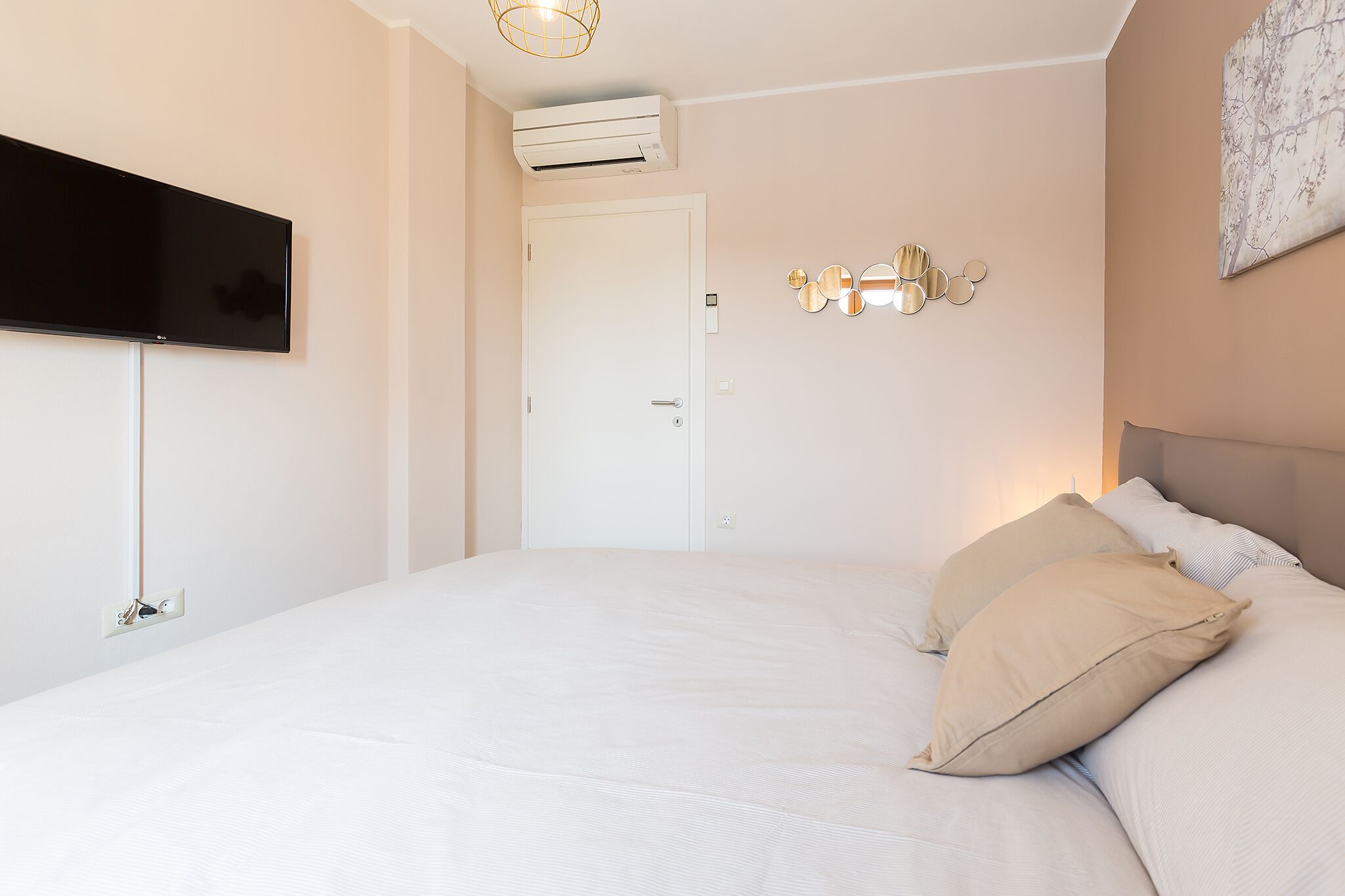 Een slaapkamer met een bed, een flatscreen televisie aan de muur, een airconditioner en een deur.