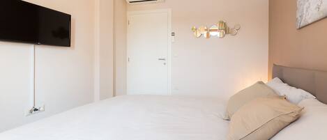 Een slaapkamer met een bed, een flatscreen televisie aan de muur, een airconditioner en een deur.