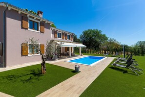 Ein zweistöckiges Haus mit Swimmingpool, Sitzgelegenheit im Freien und einem gepflegten Rasen.