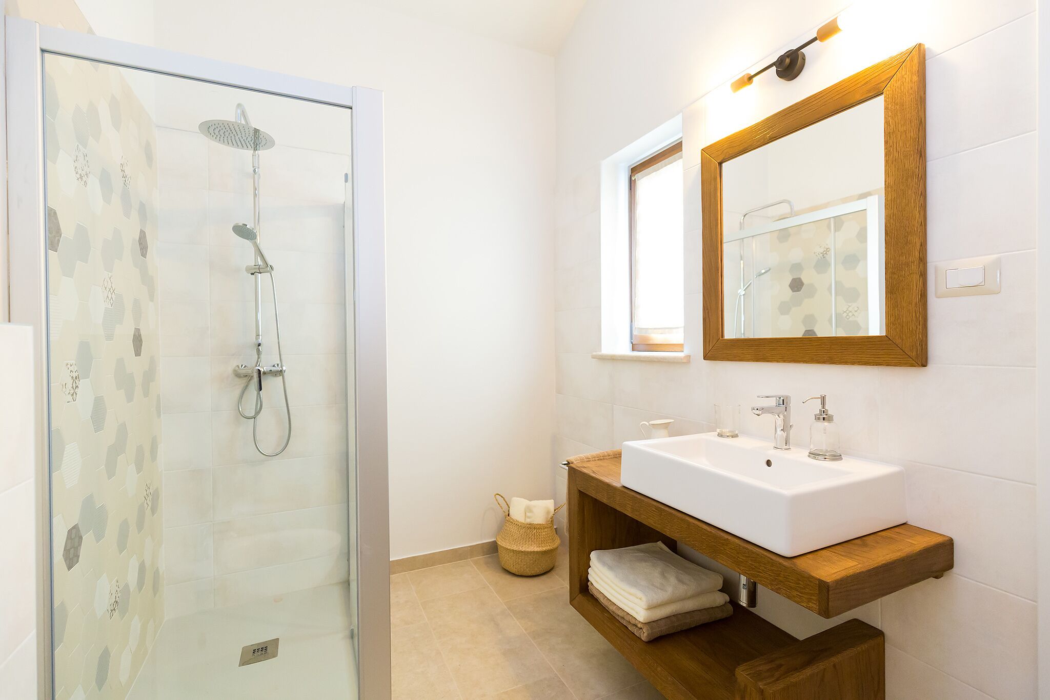 A modern bathroom with a glass-enclosed shower, a wooden vanity with a white sink, and a large mirror above the sink.