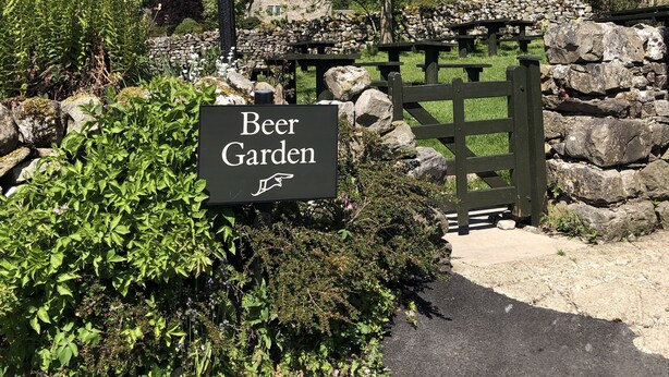 Segnaletica per un birrificio all'aperto, con un muro di pietra e un lampione in primo piano.