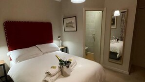 Una camera d'albergo con un letto grande, una testiera rossa, un comodino con una lampada, un quadro appeso al muro e uno specchio che riflette la stanza.