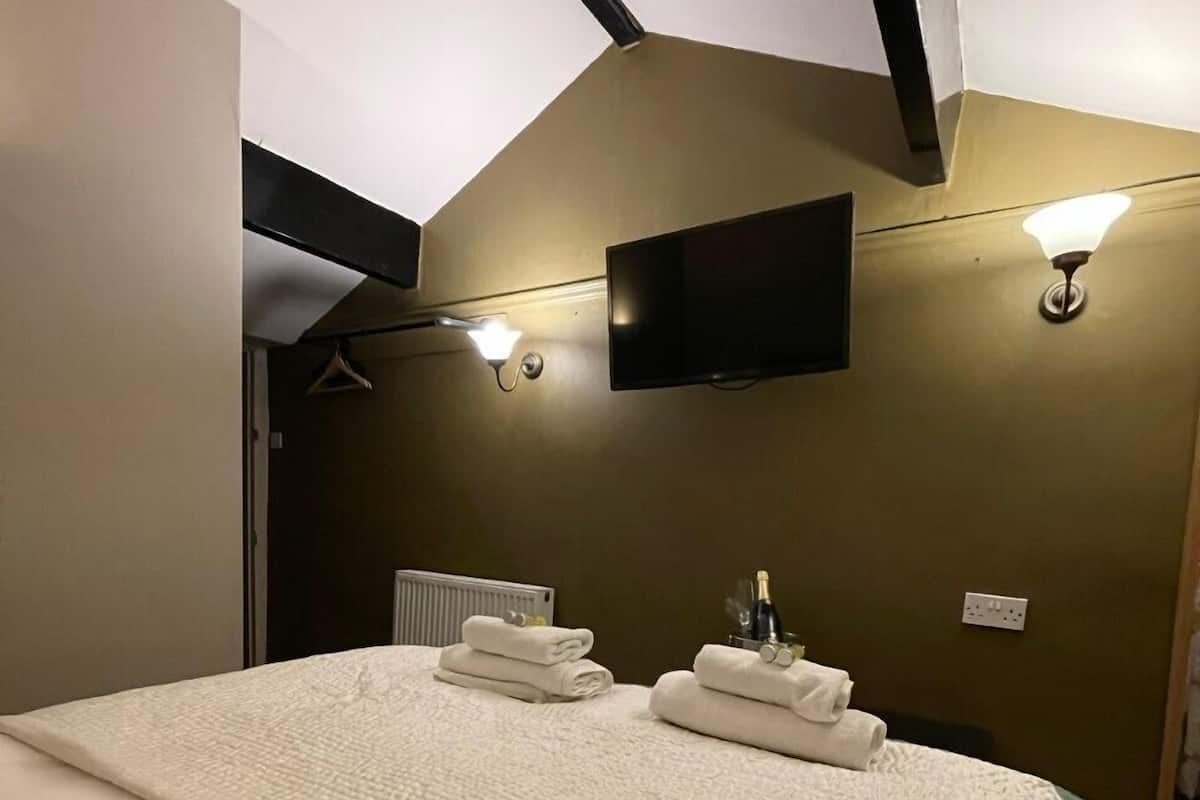 A hotel room with a large bed, a flat-screen TV mounted on the wall, and two wall-mounted light fixtures.