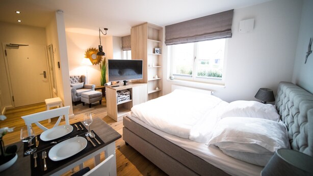 Un dormitorio moderno con una cama grande, un televisor, una zona de comedor con mesa puesta y una ventana con vistas.