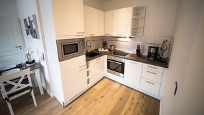 Una cocina moderna con armarios blancos, horno empotrado, microondas y cafetera.