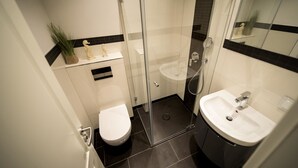 Un baño moderno con ducha de vidrio, inodoro blanco y lavamanos con espejo.