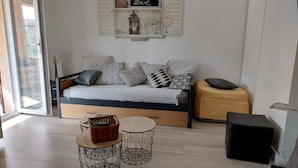 A modern bedroom with a bed, two side tables, a small ottoman, and a wall-mounted shelf with decorative items. - Quiet home in the 2-star Mimosa City (Mandelieu-la-Napoule)