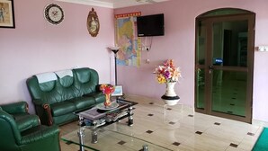 A living room with a green sofa, a coffee table with magazines, a vase of flowers, a map on the wall, and a television. - Nabegyi Hotel (North Legon)