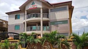 A multi-story building with a balcony on the second floor, a stone facade, and a sign indicating it is a hotel. - Nabegyi Hotel (North Legon)