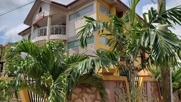 A multi-story building with a balcony, surrounded by lush greenery. - Nabegyi Hotel (North Legon)