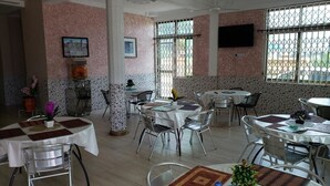 A dining area with multiple round tables, chairs, and a central pillar. - Nabegyi Hotel (North Legon)