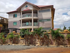 A multi-story building with a stone facade, balconies, and a sign indicating a restaurant. - Nabegyi Hotel (North Legon)