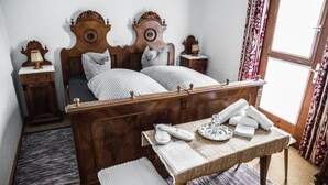 Un dormitorio tradicional con una cama de madera, dos mesitas de noche, una mesilla con lámpara y una ventana con cortinas.