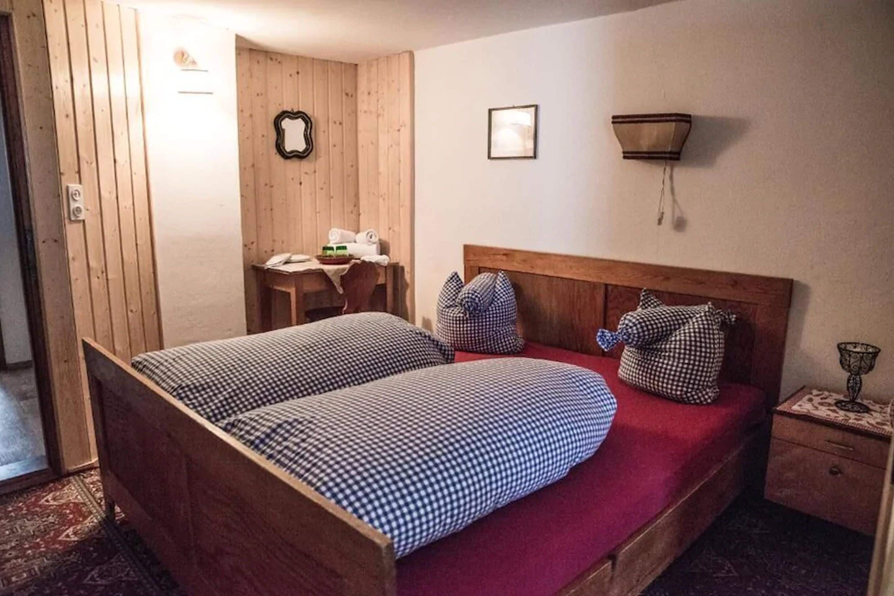 Una habitación con una cama de madera, una mesita pequeña con una silla, un espejo en la pared y una mesita de noche con una lámpara.