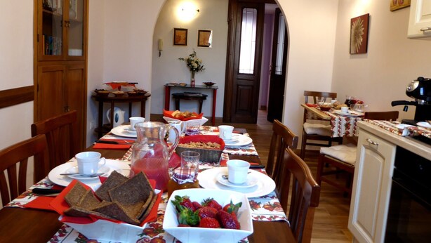 Un coin repas avec une longue table dressée pour le petit-déjeuner, comprenant du pain, des fraises et une carafe.