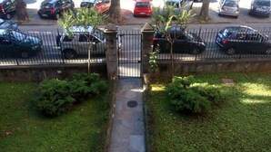 Un parking clos, avec plusieurs voitures garées le long d’une clôture, entouré d’arbres et de verdure.
