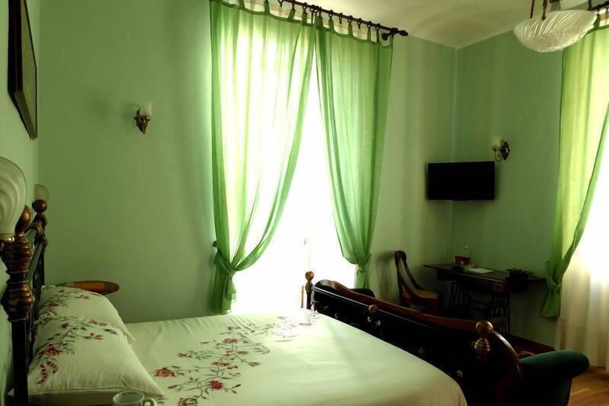 A bedroom with a bed, a chair, a desk, a television, and curtains.