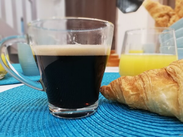 Lasissa on tummaa nestettä, mahdollisesti kahvia, ja sen vieressä on croissant sinisellä, kuvioidulla alustalla.
