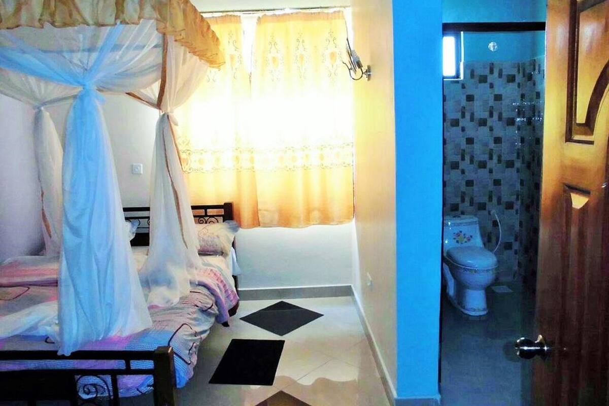 Un dormitorio con cama con dosel, una mesita de noche y un ventanal con cortinas.