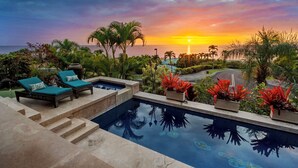 A pool area with lounge chairs and a view of the sunset over the ocean. - 🏖️Ocean View Kona Home | Saltwater Pool + Private Suites (Kailua Kona)
