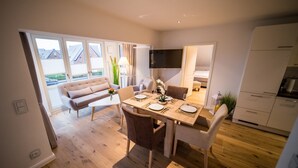 Un comedor moderno con una mesa de madera para cuatro personas, un sofá y un televisor montado en la pared.