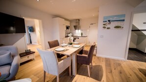 Una cocina moderna con armarios blancos, una mesa de comedor lista para cuatro personas y vista al mar a través de la ventana.