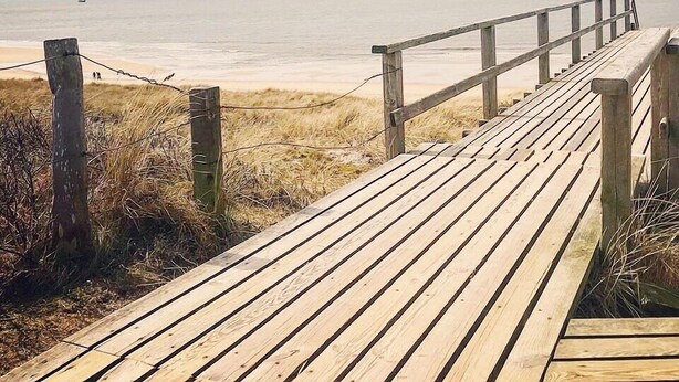A wooden boardwalk leading to a beach with a wooden railing on one side. - Abendsonne (Sylt)