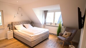 A bedroom with a bed, nightstand, chair, and window. - Abendsonne (Sylt)