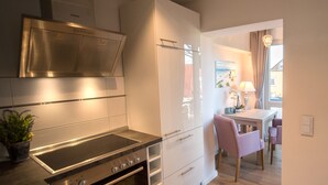A modern kitchen with stainless steel appliances, a dining area with a table and chairs, and a view of the outside through a window. - Abendsonne (Sylt)