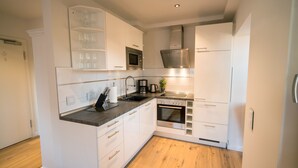 A modern kitchen with white cabinetry, a built-in microwave, a stainless steel range hood, and a wood floor. - Abendsonne (Sylt)