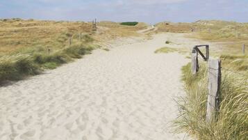 Un sendero arenoso que atraviesa un paisaje de dunas con una valla de madera a la derecha.